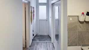 En smal hall med en dörr längst in, en kakelbeklädd vägg med en handduksdispenser och ett trägolv.