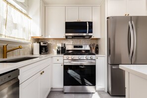 Une cuisine moderne avec des meubles blancs, un réfrigérateur en acier inoxydable, un four à micro-ondes, une cuisinière et un lave-vaisselle.