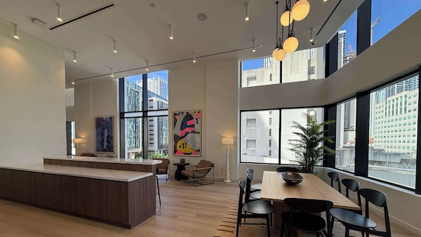 Un intérieur moderne avec un îlot central, un coin repas et de grandes fenêtres offrant une vue sur la ville.