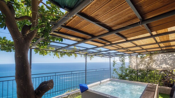 Un jacuzzi privado con vista al océano, una pérgola y un árbol.