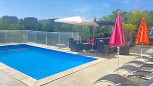 A rooftop pool with clear blue water, surrounded by a glass enclosure, and furnished with outdoor seating and umbrellas. - Beautiful house with private pool Beaujolais - 35 min from Lyon (Gleizé)