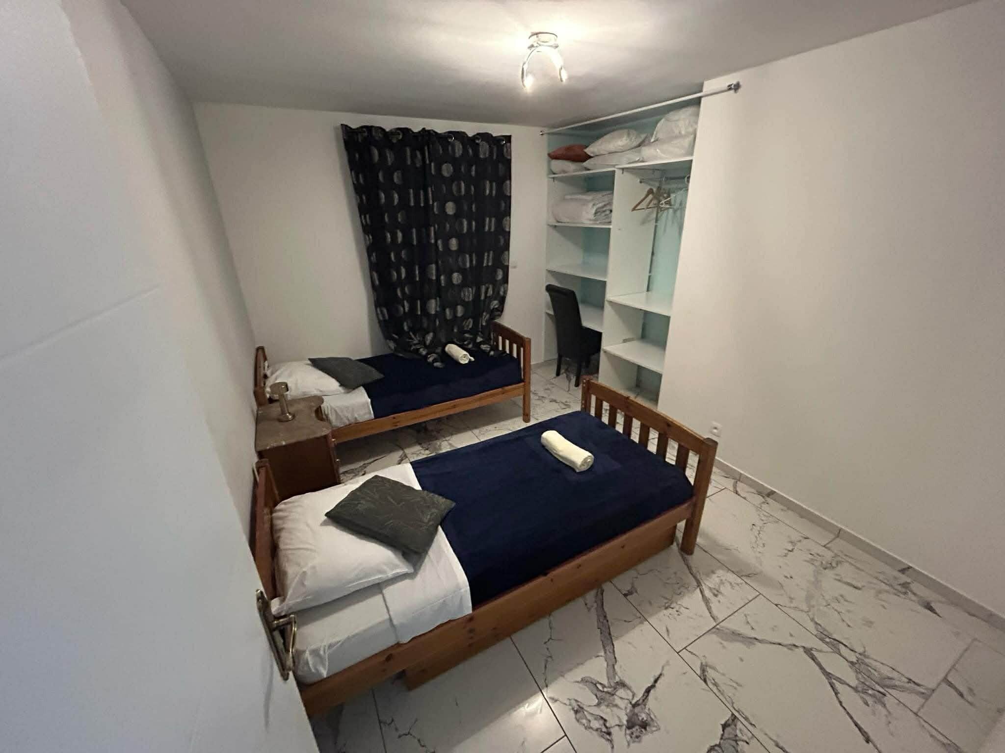 A dormitory room with two wooden beds, a chair, a desk, and a wardrobe.