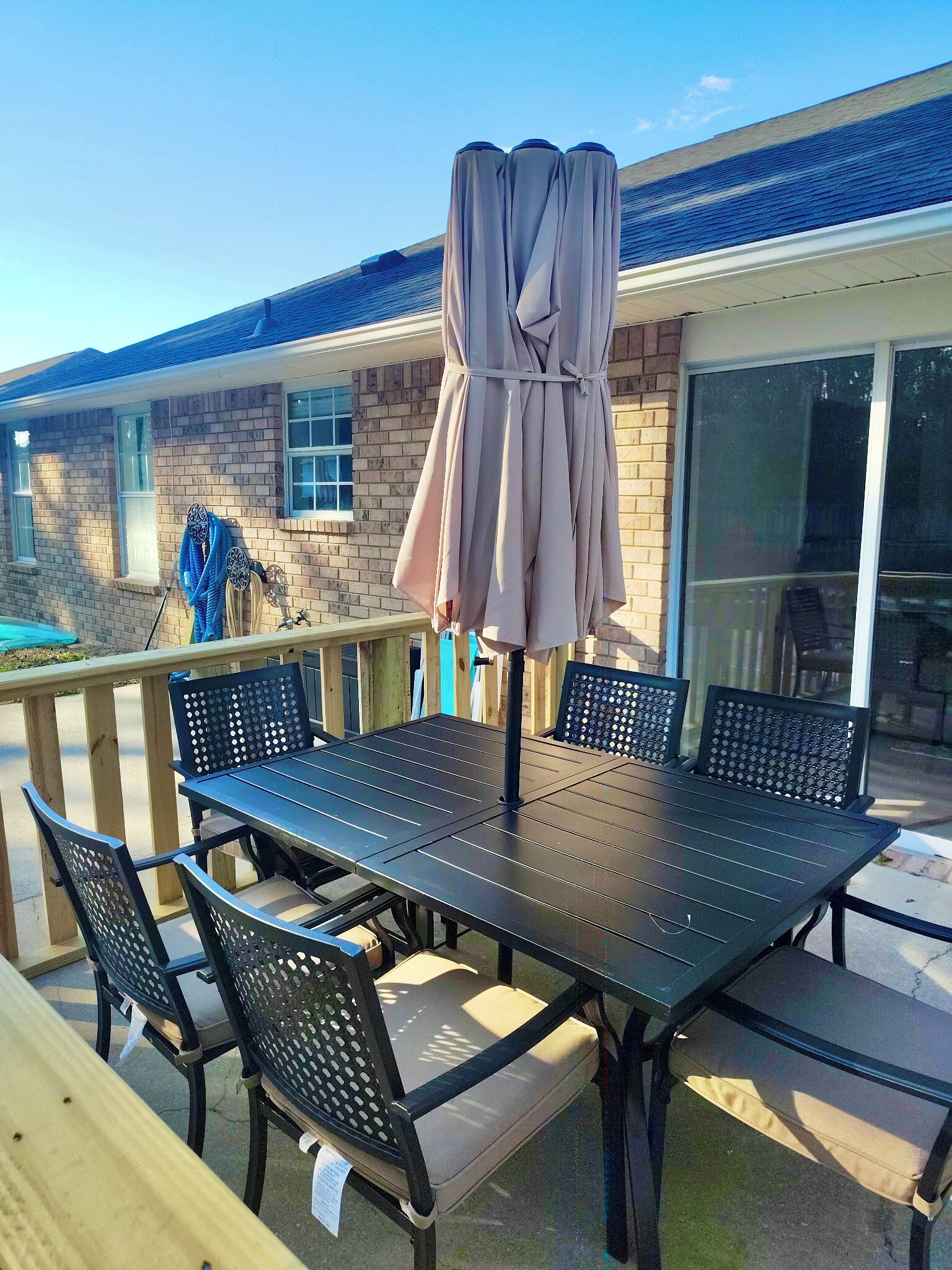 An outdoor patio with a table and chairs, a covered umbrella, and a view of a house with a brick exterior and a window.