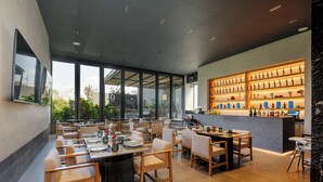 A modern restaurant with a bar area, large windows, and a variety of seating arrangements. - Be grand del Valle by Wynwood House (Mexico City)