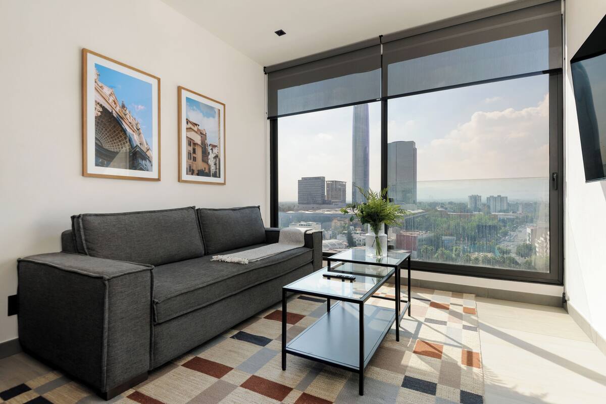 Una sala de estar moderna con un sofá, una mesa de centro de vidrio y un ventanal que ofrece vistas a la ciudad.