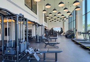 Ein Fitnessstudio mit verschiedenen Trainingsgeräten, darunter Laufbänder und Kraftmaschinen, in einem großzügigen Raum mit großen Fenstern, die viel Tageslicht hereinlassen.