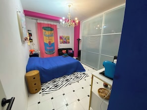 A bedroom with a bed, a dresser, a chair, a window, and a curtain. - POP ART ROOM (Milano)
