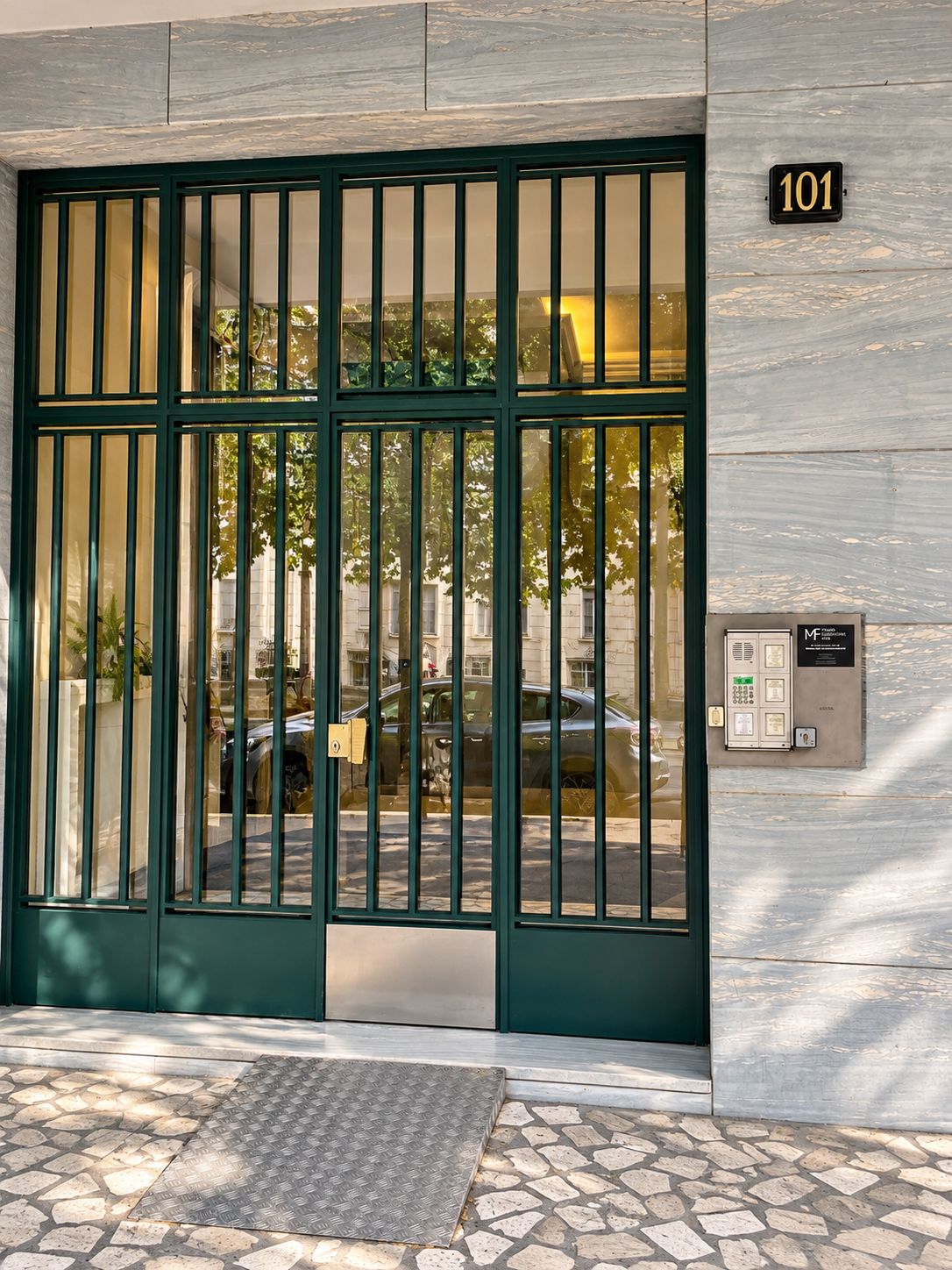 L’entrée d’un hôtel, avec un portail métallique vert, une plaque portant le numéro « 101 » et un clavier permettant d’accéder aux chambres.