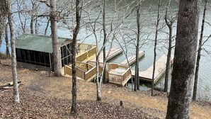 Eine Holzhütte mit Gründach und einer über einen See reichenden Holzterrasse, umgeben von Bäumen.