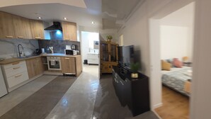 A modern kitchen with wooden cabinets, a black stove, and a microwave. There is a dining area with a bed visible in the background. - Poolside cottage (Oinville-sur-Montcient)