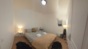 Une petite chambre bien éclairée, avec un lit, des tables de chevet et une commode.