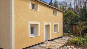 A two-story building with a yellow exterior, two small windows, and a stone pathway leading to the entrance. - Poolside cottage (Oinville-sur-Montcient)