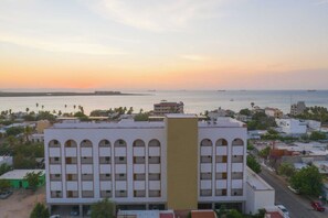 Rannalla sijaitseva rakennus, jossa on useita parvekkeita, tasakatto ja näkymä merelle.