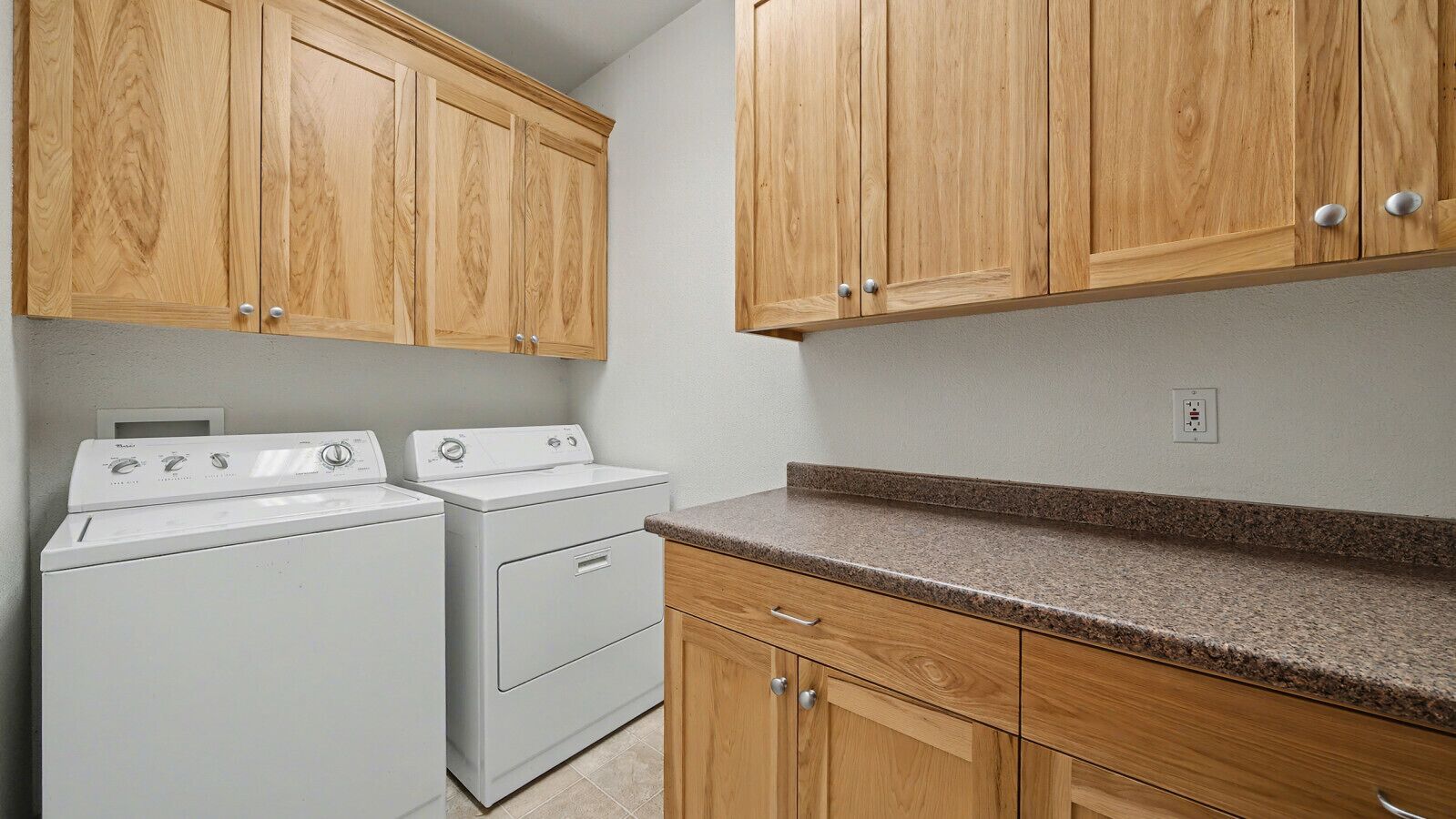 A laundry room with two white washing machines, wooden cabinets, and a granite countertop.