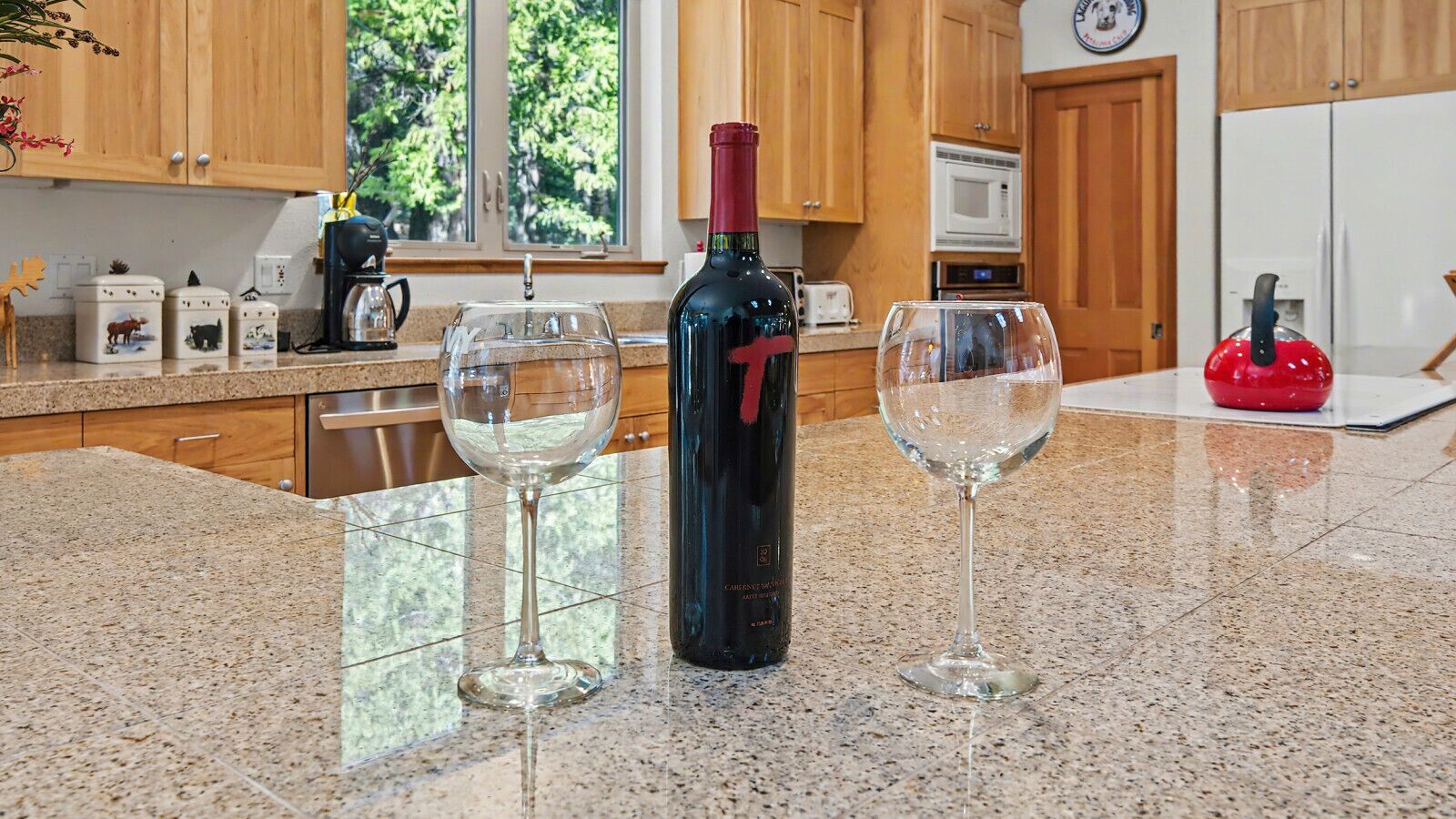 A kitchen with granite countertops, wooden cabinets, a wine bottle, and two wine glasses.