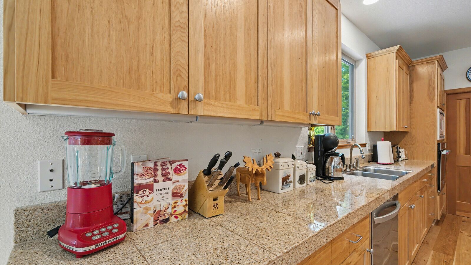 A kitchen with wooden cabinets, a granite countertop, a red blender, a coffee maker, and a toaster.