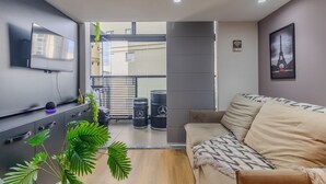 A modern living room with a flat-screen TV, a sofa, a coffee table, and a potted plant. - Studio na Lapa Varanda Academia e Coworking (São Paulo)