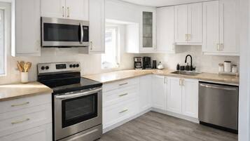 A modern kitchen with white cabinetry, stainless steel appliances, and a wooden countertop.