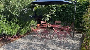 A gravel patio with red metal chairs and a table, surrounded by dense foliage. - Le Nid - Domaine de la Tour - New apartment for 6 people (Fleury)