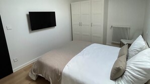 A bedroom with a bed, a television mounted on the wall, a radiator, and a ceiling light. - Le Nid - Domaine de la Tour - New apartment for 6 people (Fleury)