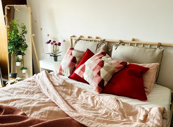A neatly made bed with a beige and red patterned pillow set, a wooden headboard, and a bedside table with a potted plant and a vase of flowers. - Sunny and Spacious Feng Shui Home in Lisbon (Lisbon)