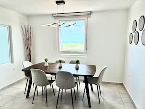 Ein Essbereich mit einem dunklen Holztisch, sechs grauen Stühlen und zwei Zimmerpflanzen.