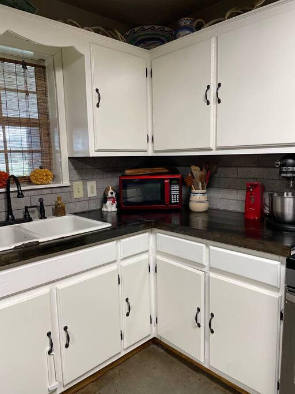 A kitchen with white cabinets, a red microwave, and a sink.