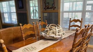 Un comedor con una mesa y sillas de madera, un espejo decorativo y una ventana con persianas.