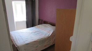 Quarto pequeno e com poucos móveis, com uma cama, um encosto de madeira e uma parede roxa.