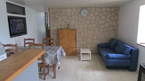Uma sala de estar com parede de pedra, um sofá azul, uma mesa de madeira com cadeiras, uma mesinha branca e um armário de madeira.