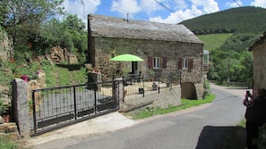 A stone building with a tiled roof, a fenced patio, and a green umbrella. - Typical Lozere house (les bondons)
