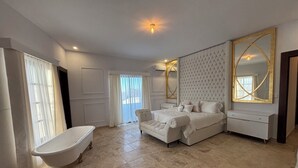 A spacious bedroom with a large bed, a vanity with a mirror, and a clawfoot bathtub.