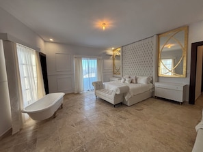 A spacious bedroom with a large bed, a vanity with a mirror, and a clawfoot bathtub.