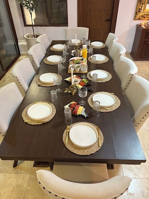A dining table set for a meal with white plates, gold-rimmed place settings, and a centerpiece of fruits and cheese.