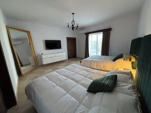 A hotel room with two beds, a TV, a dresser, and a chandelier.