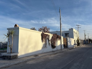 A white building with a flat roof, a small window, and a door. There are power lines and a utility pole visible.