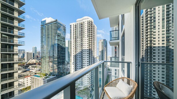 Un balcon avec un fauteuil en osier et une vue sur les immeubles de grande hauteur.