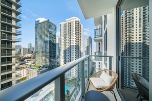 Een balkon met een rieten stoel en uitzicht op hoge gebouwen.