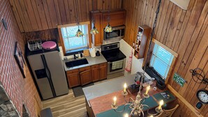 Cocina estilo cabaña con paredes de madera, refrigerador, estufa, microondas y un comedor con candelabro.