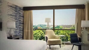 Habitación de hotel con una cama grande, dos sillas, un escritorio y vistas a zonas verdes y edificios.