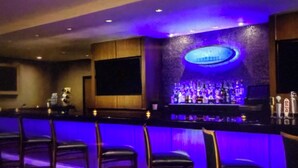 Zona de bar con mostrador, taburetes y una estantería llena de botellas.