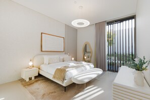 A modern bedroom with a large bed, bedside tables, a bedside lamp, a mirror, and a window with curtains. - 4BR Coastal Haven w/  Private Pool | Al Zorah (Ajman)