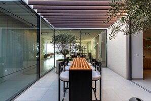 A modern dining area with a long table, chairs, and a glass partition. - 4BR Coastal Haven w/  Private Pool | Al Zorah (Ajman)