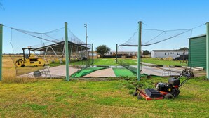 A fenced outdoor area with a lawnmower, a yellow vehicle, and a green shed. - Rural Ranch Stay w/ Cricket & Turf Fields (Wallis)