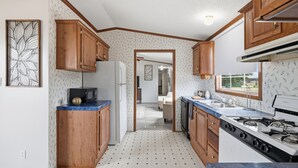 A compact kitchen with wooden cabinets, a microwave, a refrigerator, and a stove. - Rural Ranch Stay w/ Cricket & Turf Fields (Wallis)