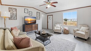 A spacious living room with a sofa, armchairs, a coffee table, and a television. - Rural Ranch Stay w/ Cricket & Turf Fields (Wallis)