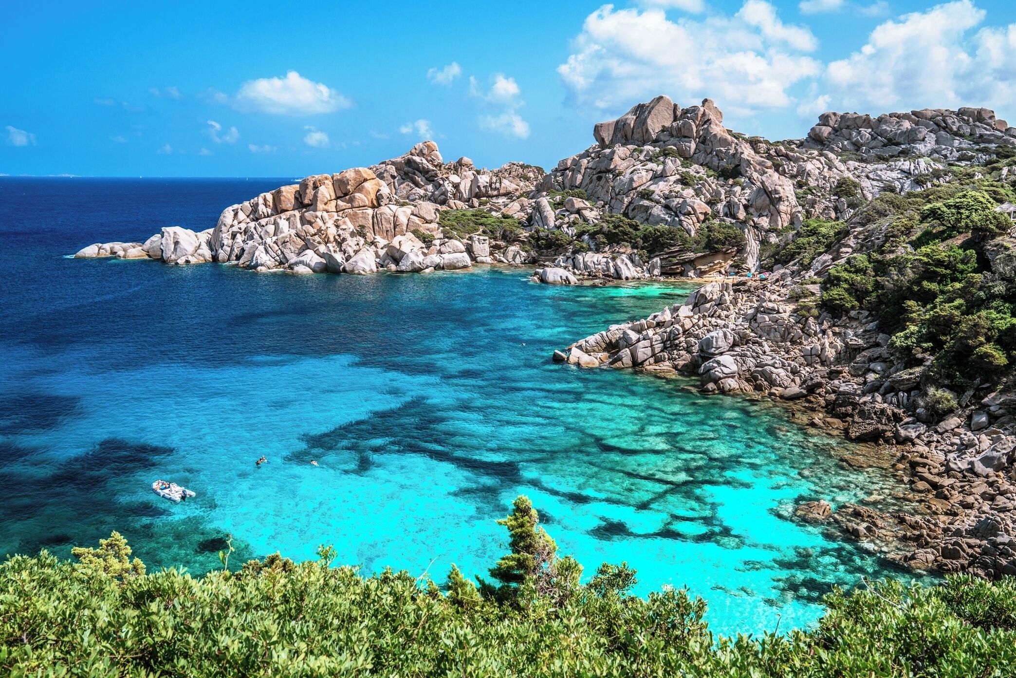 A rocky coastal landscape with clear turquoise waters and lush greenery.