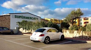Un parking avec une voiture blanche garée devant un bâtiment portant l’inscription « SUPERMERCATO ».