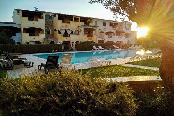 A pool area with lounge chairs and a building with multiple balconies.