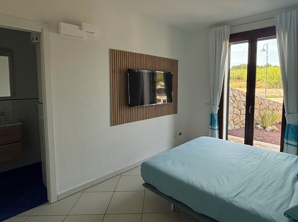 Camera da letto con un letto, una TV montata a parete, bagno con lavandino e vista panoramica attraverso una porta in vetro.